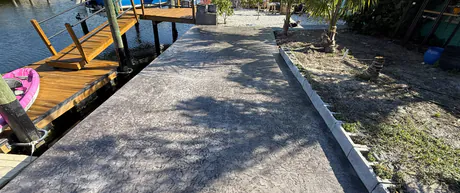 Stamped concrete walkway running out to a covered residential boat dock over the water.