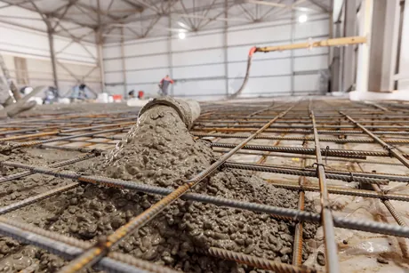 Concrete discharging from a pump hose onto a tied rebar mat during a structural slab pour inside a steel-framed commercial building.