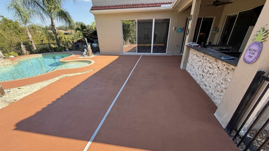Custom terracotta brown knockdown finish concrete pool deck and patio overlay with an integrated white deck drain system next to an outdoor kitchen bar, completed by Crego Concrete.